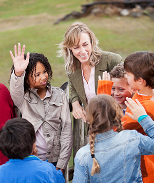 Teacher (50s) with multi-ethnic group of elementary school children at zoo, standing on observation deck overlooking animal exhibit.